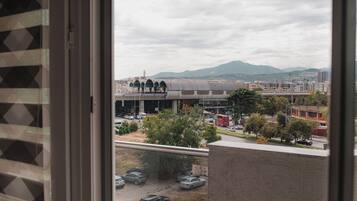 Vista da una finestra su un paesaggio urbano con un grande edificio con cupola e strutture ad arco, un'autostrada con veicoli e montagne in lontananza.
