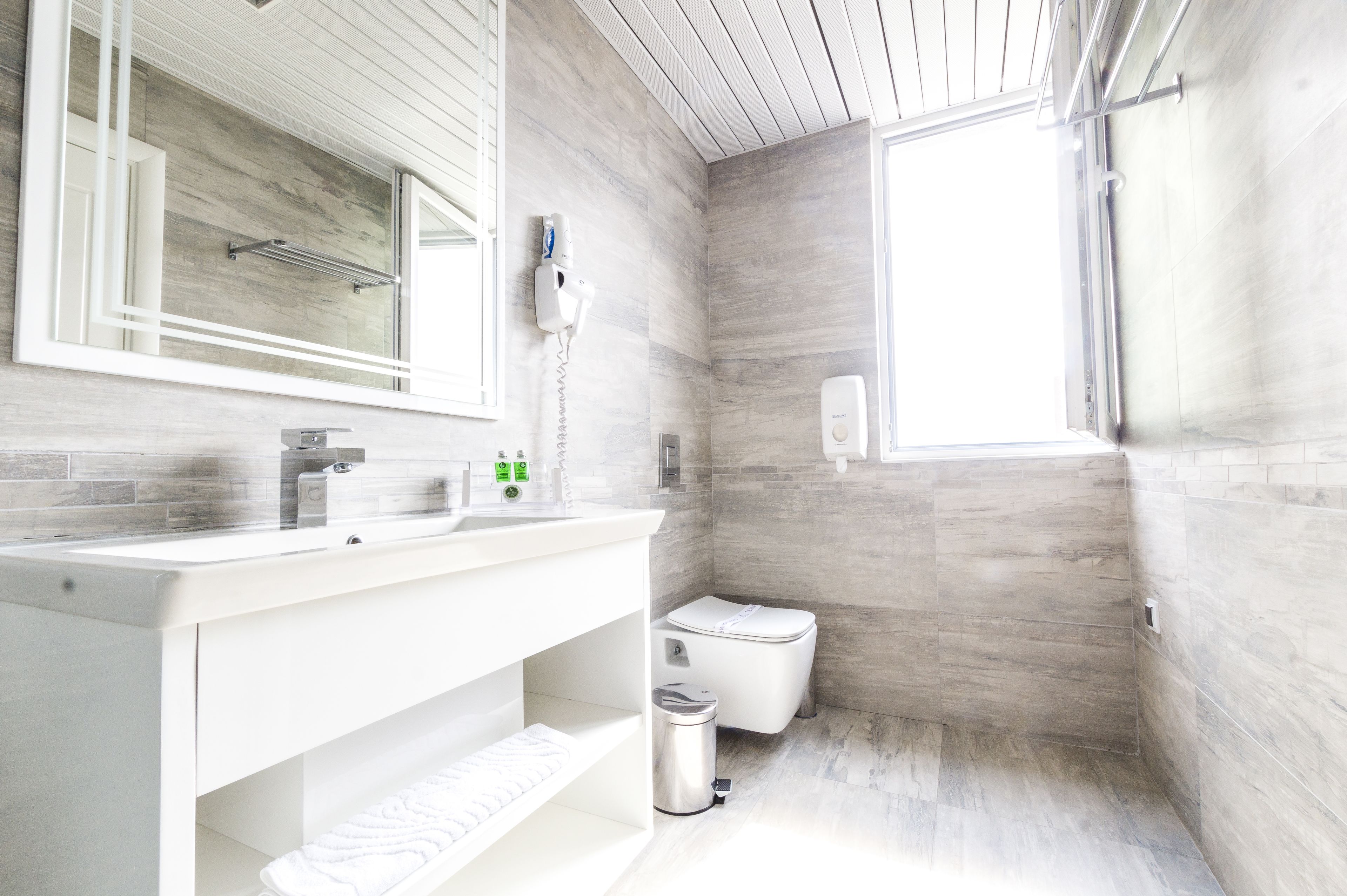 Un baño moderno con un espejo grande, tocador blanco y un inodoro.