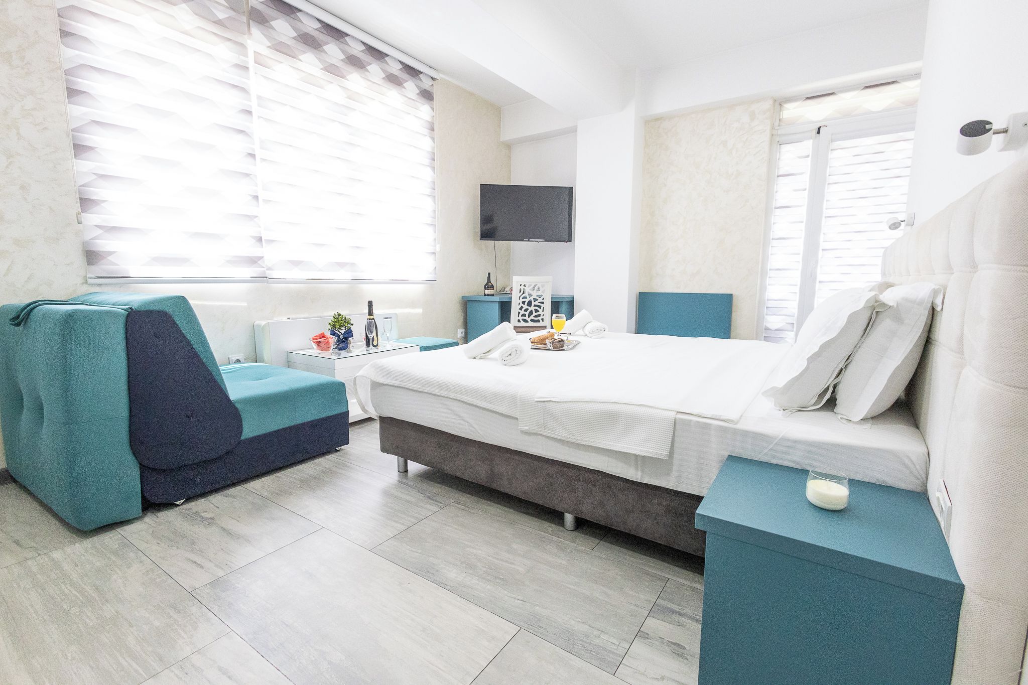 Une chambre d’hôtel moderne équipée d’un lit, d’un coin salon, d’une télévision et d’une fenêtre avec des stores.