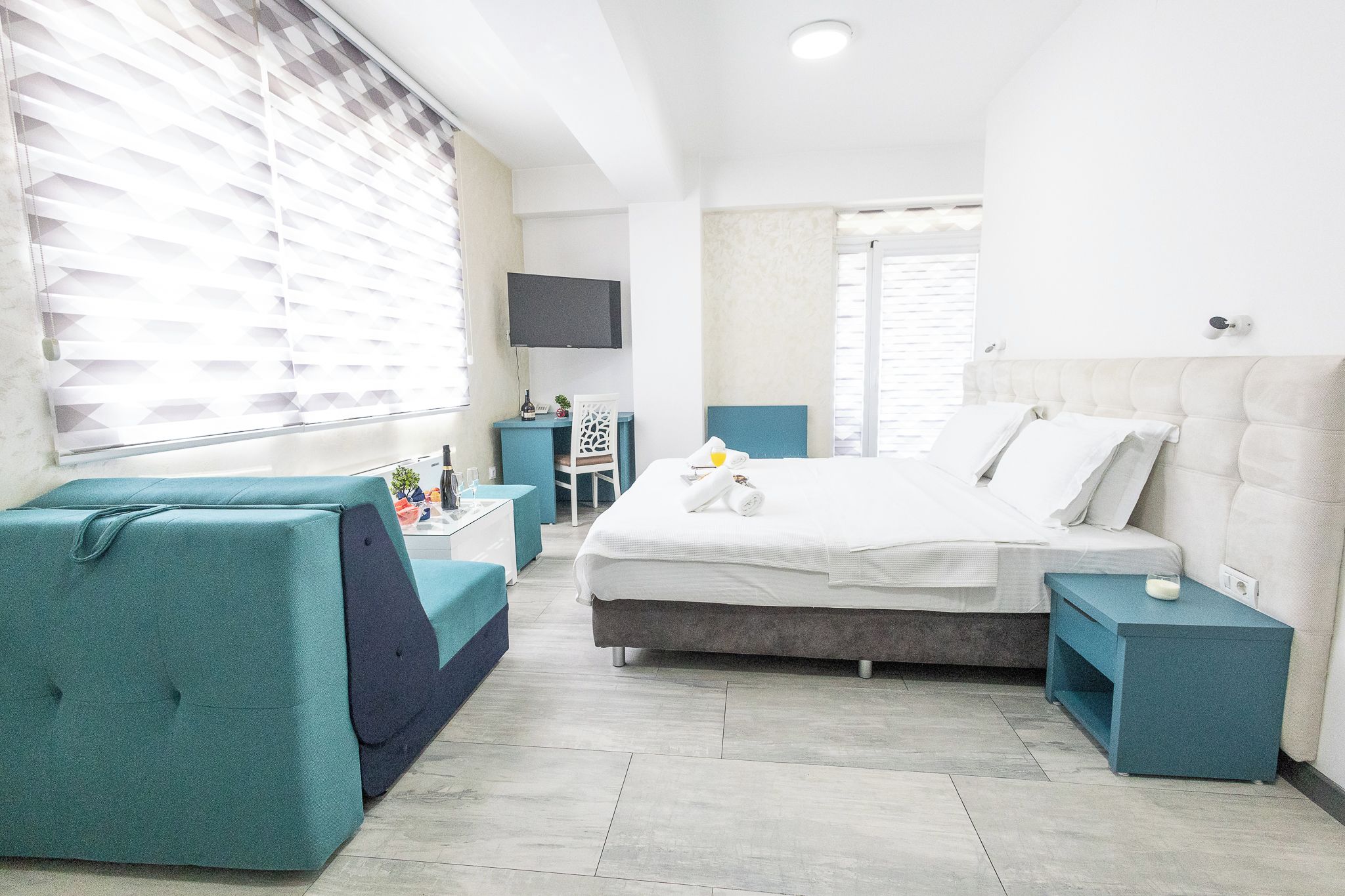A modern hotel room with a bed, a seating area, a desk, and a television.