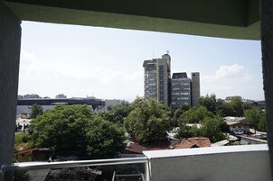 Un edificio alto con varios pisos y techo plano, rodeado de árboles y edificios más pequeños.