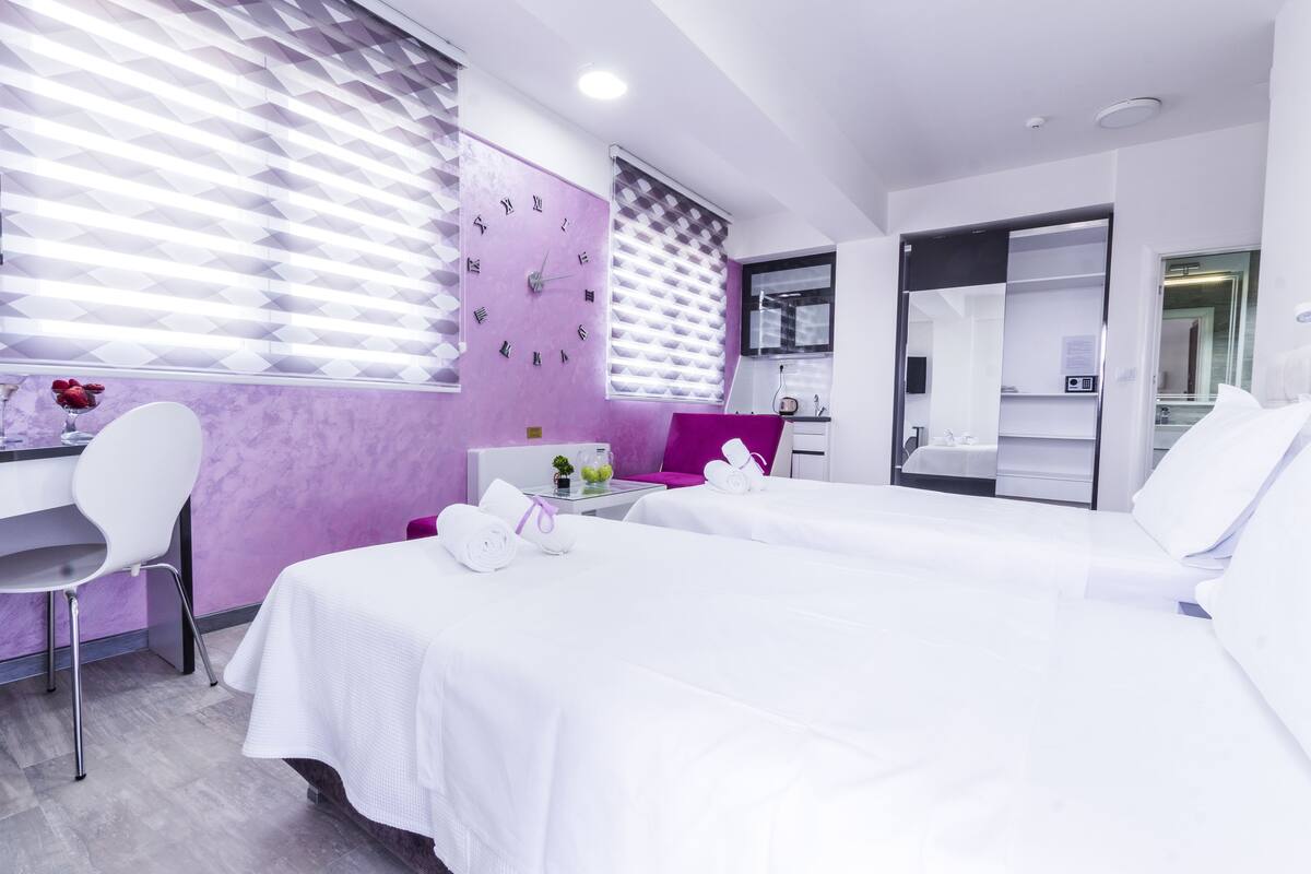 A modern hotel room with two beds, a desk, and a chair.