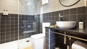 Een moderne badkamer met een douche met glazen wand, een wit wastafelmeubel en een zwart betegelde wand.