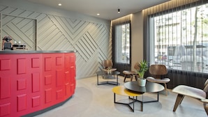 Een modern ingerichte receptiebalie met een rode toonbank, een wand in herringbone-patroon en een zithoek met een ronde tafel en stoelen.