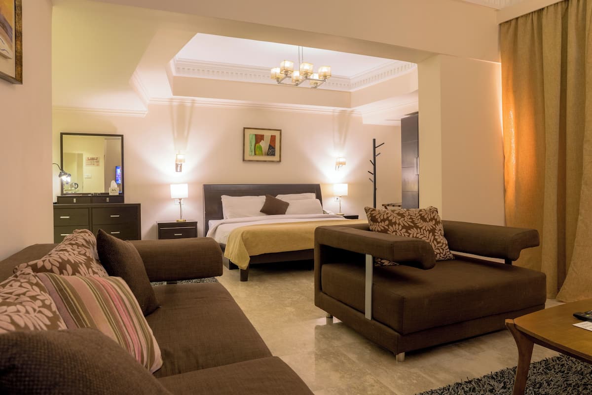 A hotel room with a bed, two sofas, a coffee table, a desk, and a mirror.