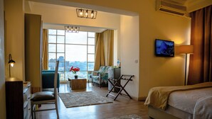 Une chambre d’hôtel avec un lit, un bureau, une chaise, une télévision, une fenêtre avec des rideaux et une vue sur la ville.