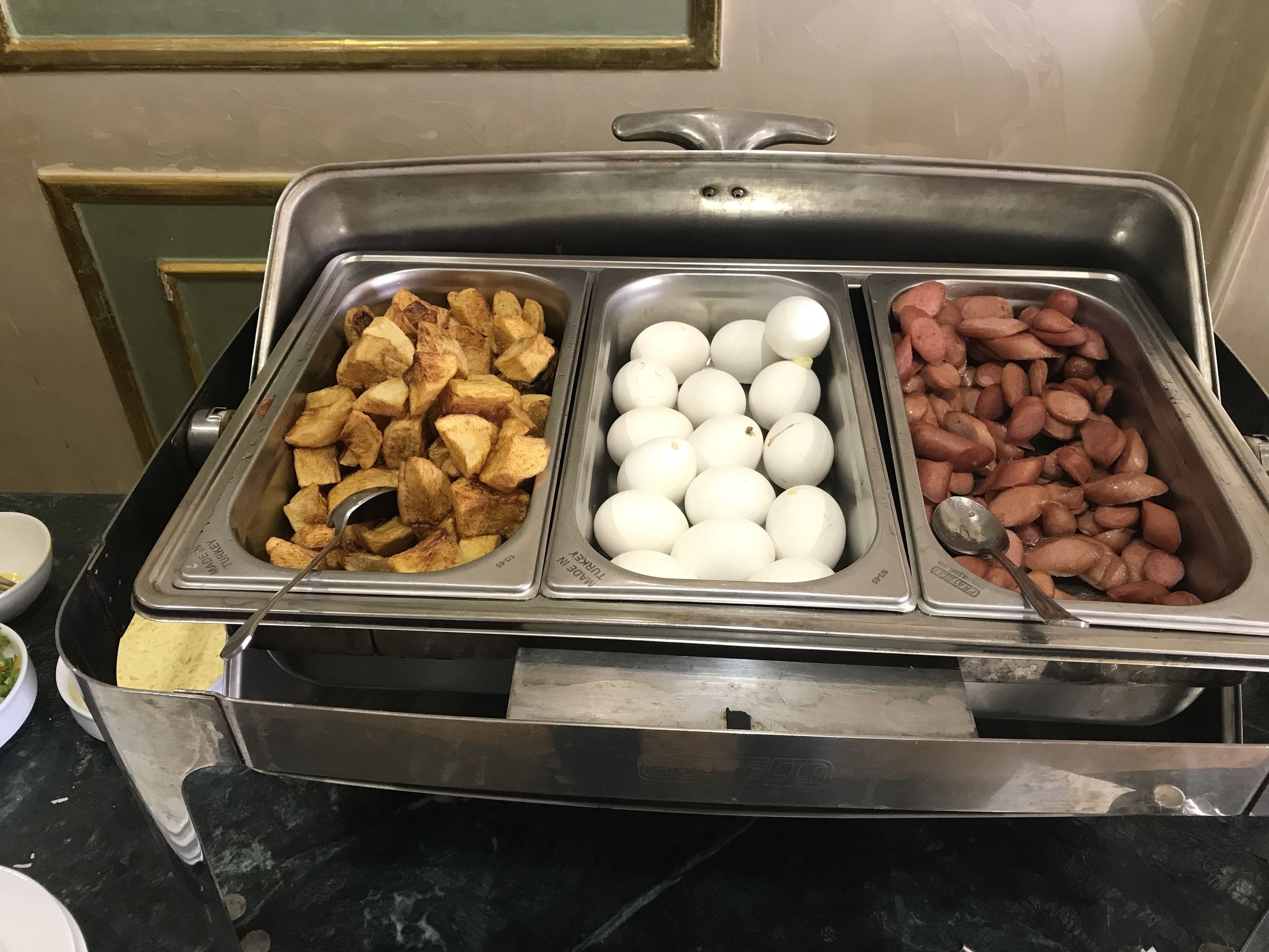 A buffet with three sections: fried potatoes, boiled eggs, and sausages.