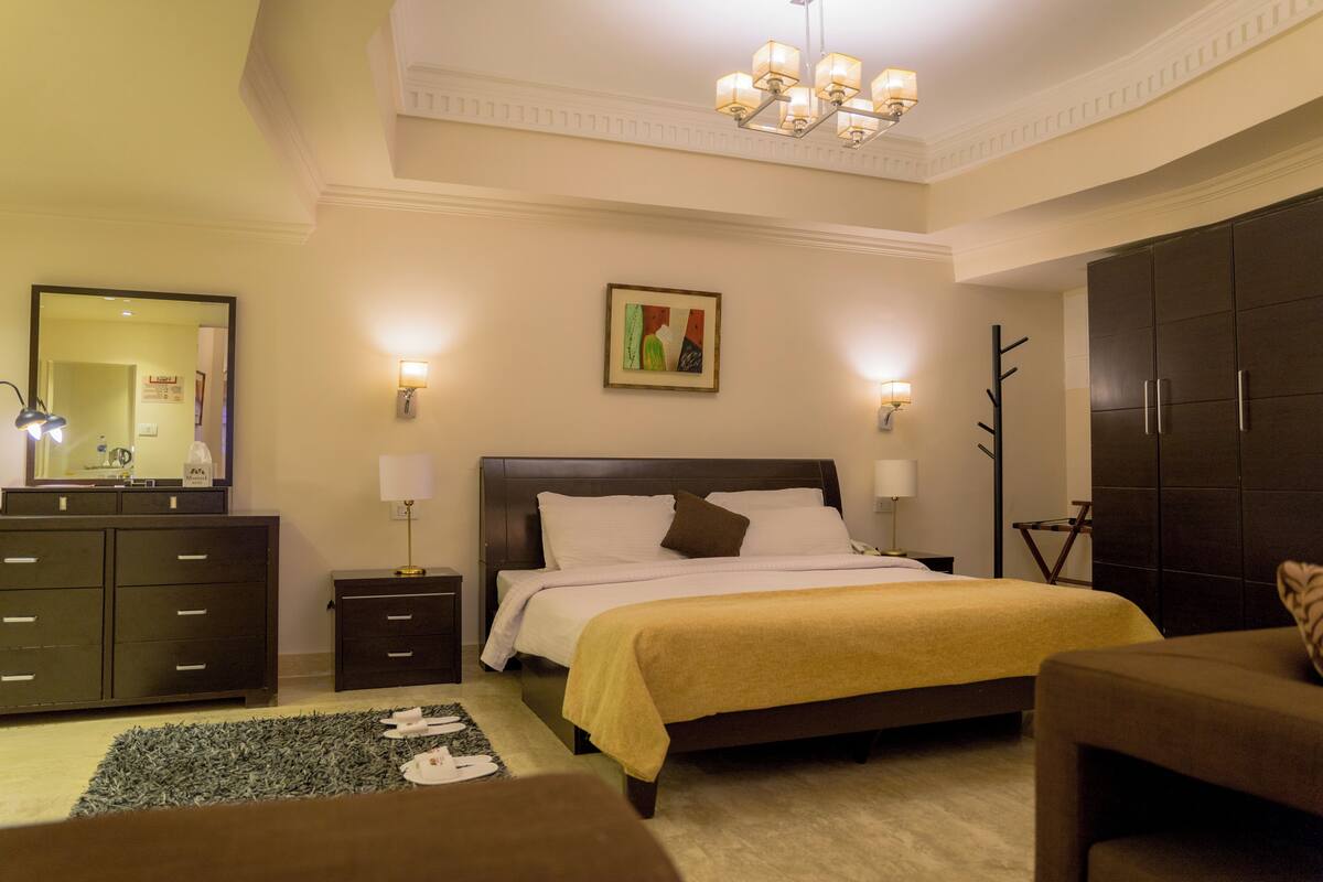 A hotel bedroom with a large bed, a dresser, a mirror, and a chandelier.