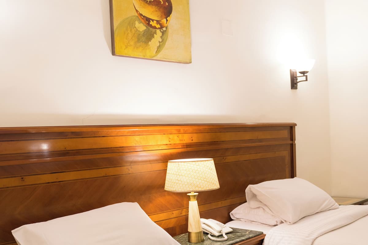 A hotel room with two beds, a wooden headboard, a bedside lamp, a telephone, and a painting on the wall.