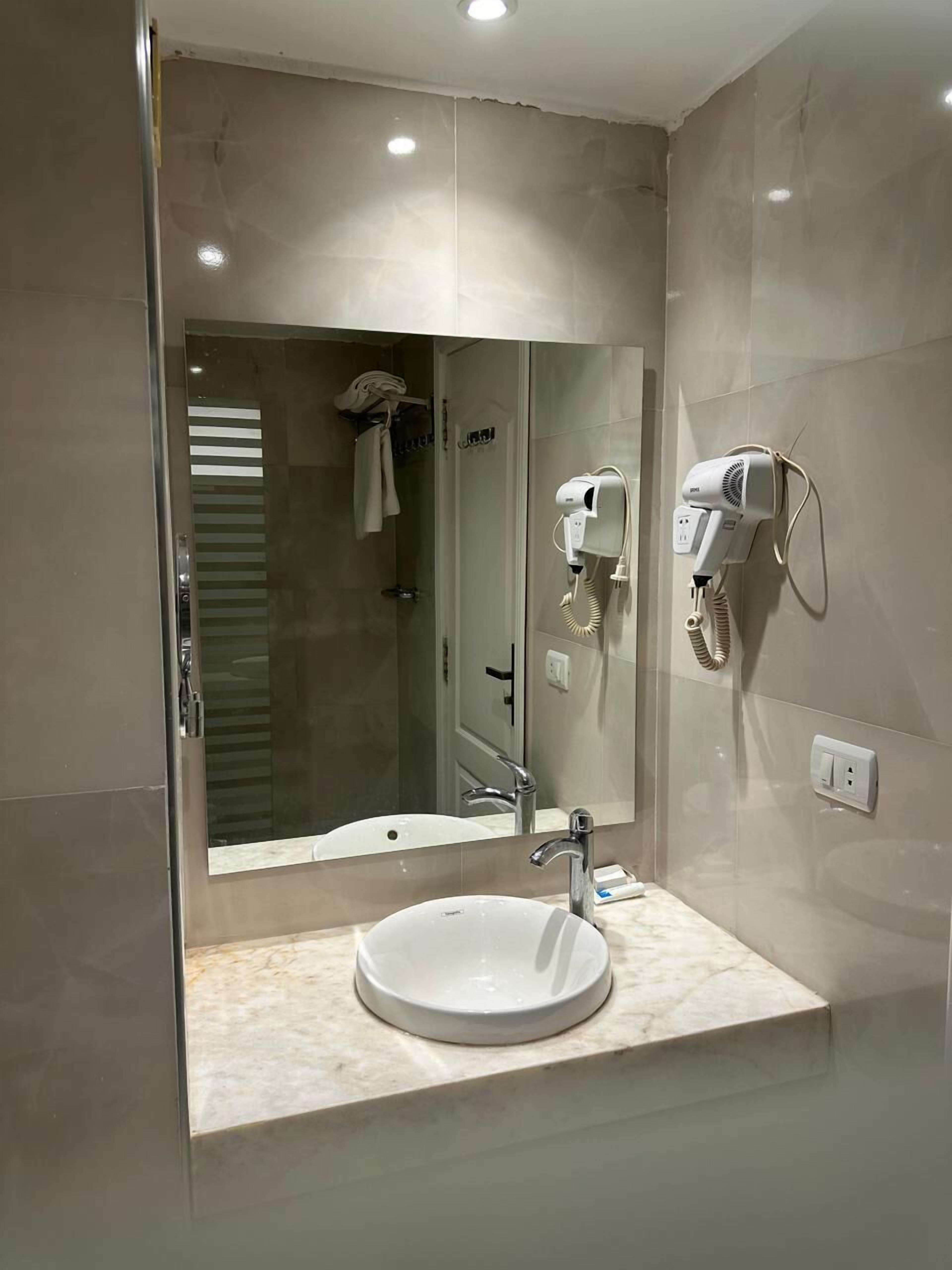 A modern bathroom with a large mirror, a sink, and a hairdryer mounted on the wall.