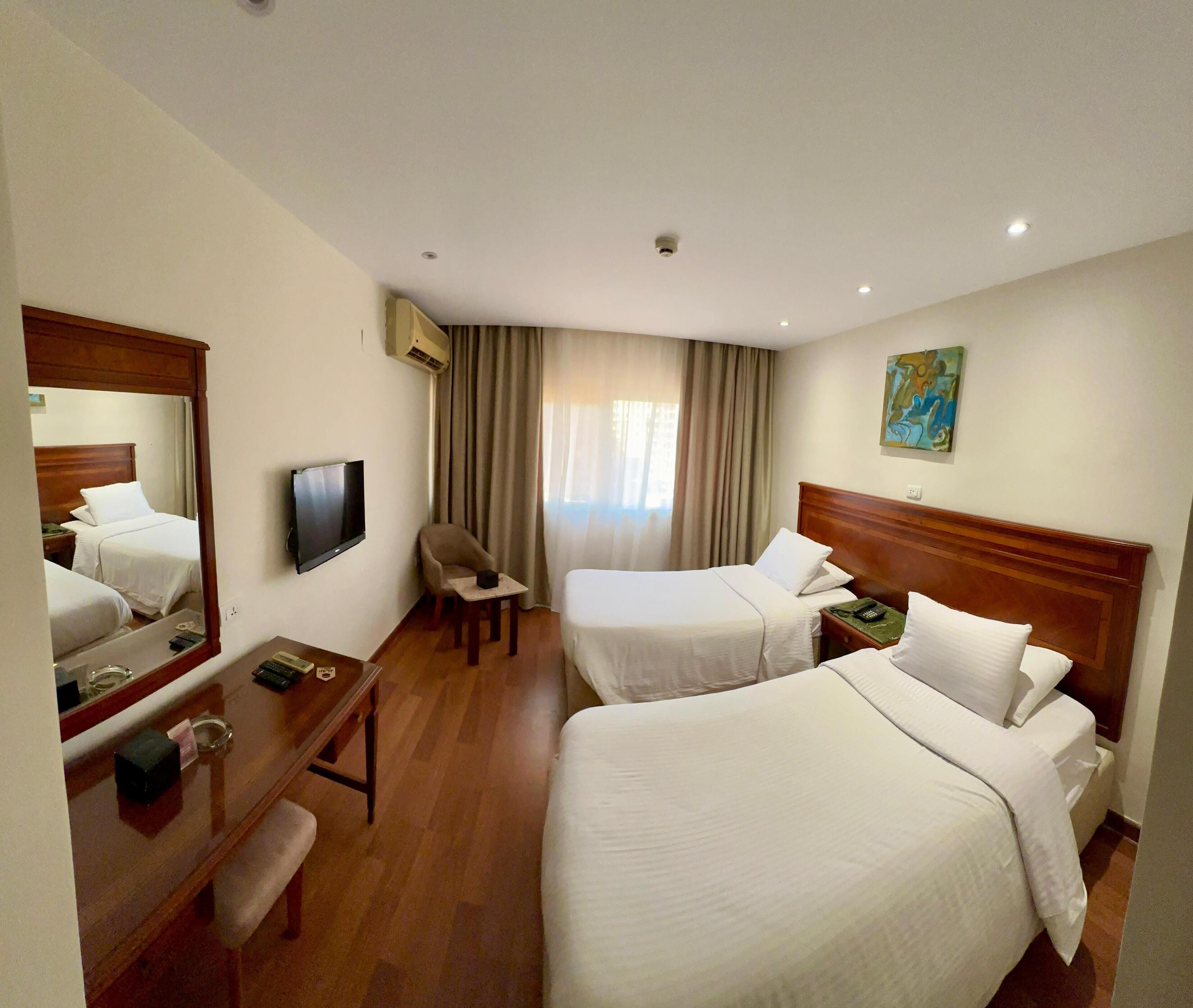 Une chambre d’hôtel avec deux lits, un bureau avec une chaise, une télévision et un tableau au mur.
