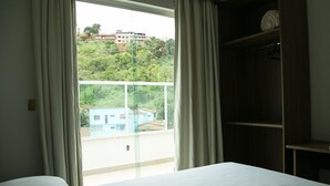 Habitación de hotel con cama, armario y ventana con vistas a edificios y zonas verdes.