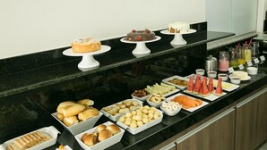 Un bufé con diversas opciones de comida, entre ellas pasteles, panes dulces y frutas.