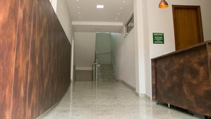 Zona de recepción de hotel con un mostrador de madera, una escalera de cristal y un letrero verde en la pared.
