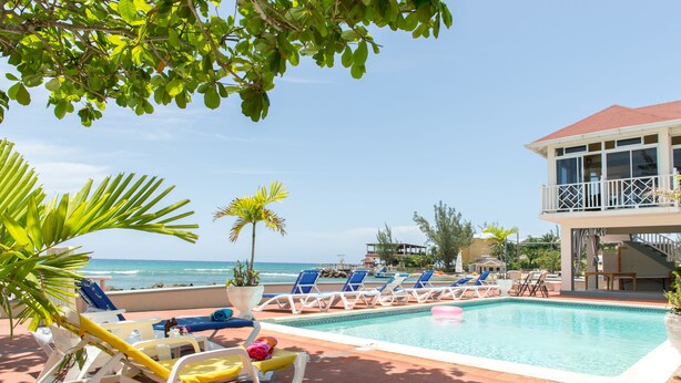 A pool area with lounge chairs and a view of the ocean. - Pipers Cove - Runaway Bay (Runaway Bay)
