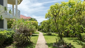 A pathway leading to a house with a red roof, surrounded by lush greenery and flowering plants. - Pipers Cove - Runaway Bay (Runaway Bay)