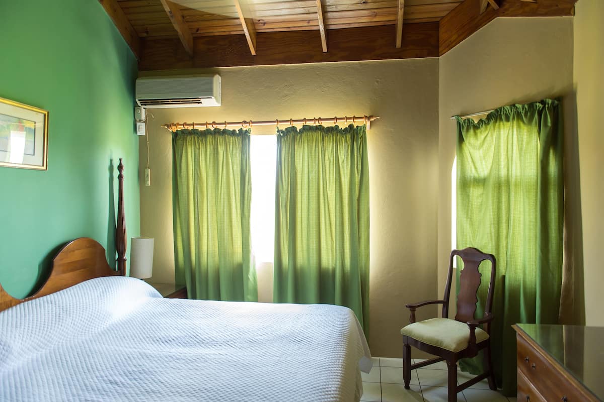 A bedroom with a bed, a chair, a dresser, and a window with green curtains.