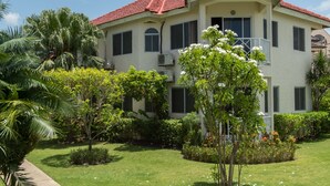 A two-story building with a red-tiled roof, surrounded by a well-maintained garden with various plants and flowers. - Pipers Cove - Runaway Bay (Runaway Bay)