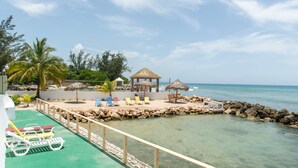 A beachside resort with a pool area, lounge chairs, a gazebo, and a rocky shoreline. - Pipers Cove - Runaway Bay (Runaway Bay)