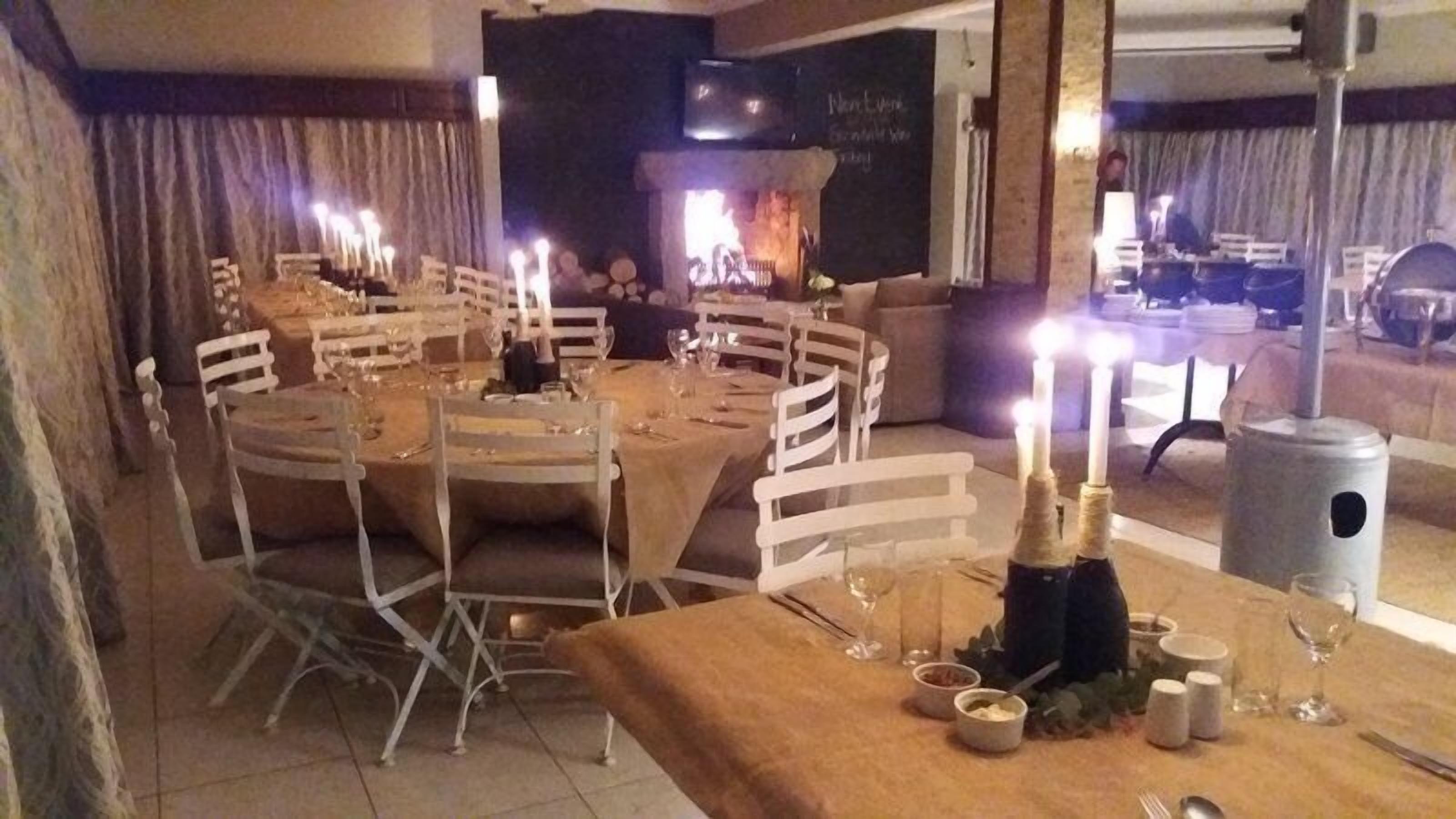 A dining area with round tables set for a meal, candles, and a fireplace in the background.