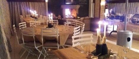 Un comedor con mesas redondas dispuestas para una comida, velas y una chimenea al fondo.