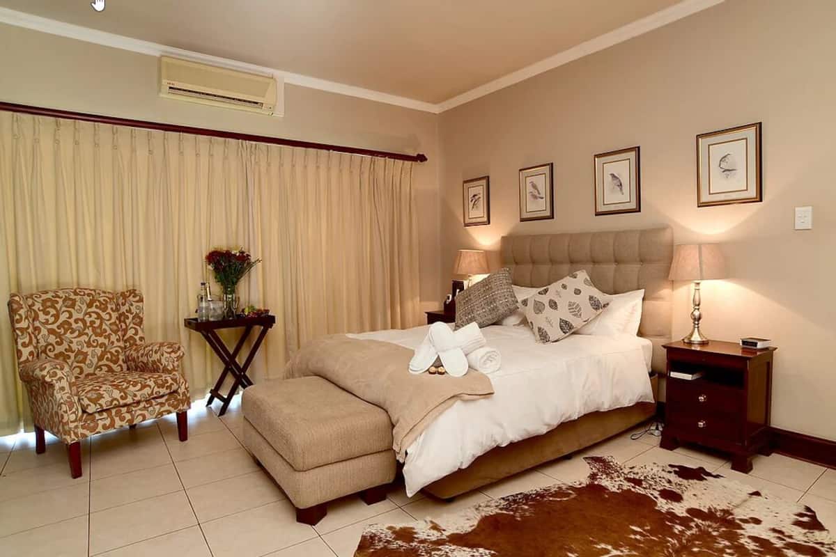 A bedroom with a large bed, a chair, a nightstand, and a cowhide rug.