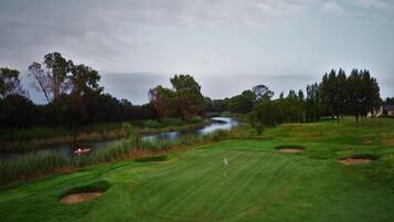 Campo de golf con un cuerpo de agua, árboles y cielo nublado.