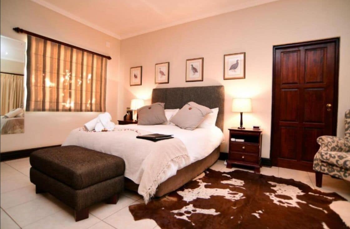 A bedroom with a large bed, a wooden nightstand, a chair, a cowhide rug, and a door.