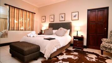 A bedroom with a large bed, a wooden nightstand, a chair, a cowhide rug, and a door.