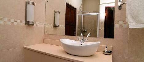Un baño con lavamanos blanco, un espejo grande y zona de ducha.