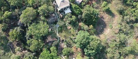 An aerial view of a property with a main building, a secondary structure, and a swimming pool surrounded by dense vegetation.
