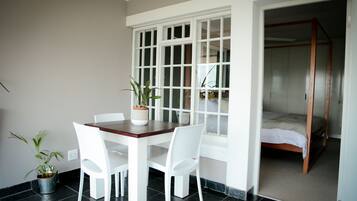 A room with a dining table, chairs, a potted plant, a window, and a bed.