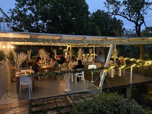 An outdoor dining area with tables and chairs, string lights, and greenery. - Mogi Boutique Hotel (Lobamba)