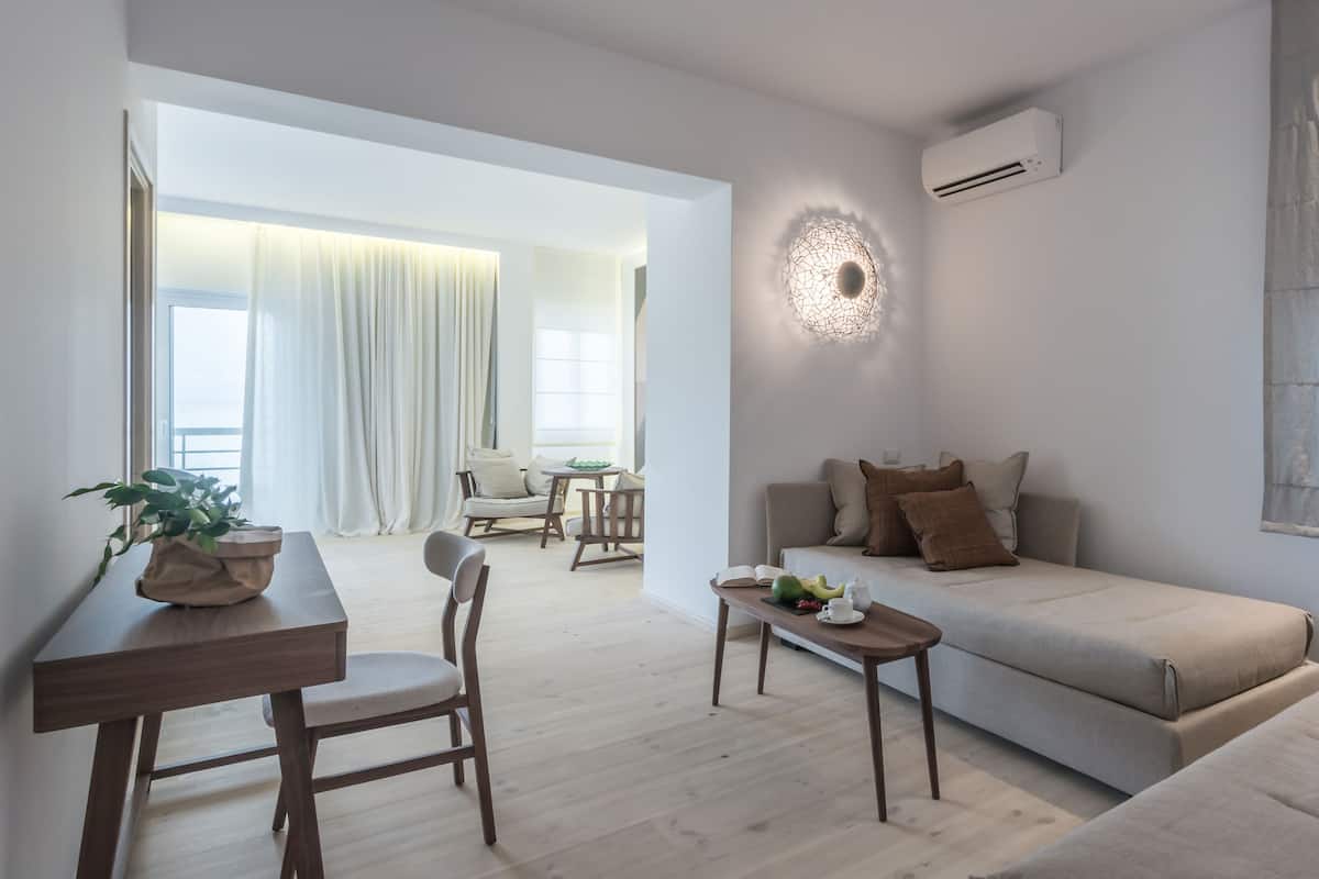 A modern living room with a sofa, a dining table with chairs, a potted plant, and a wall-mounted air conditioner.