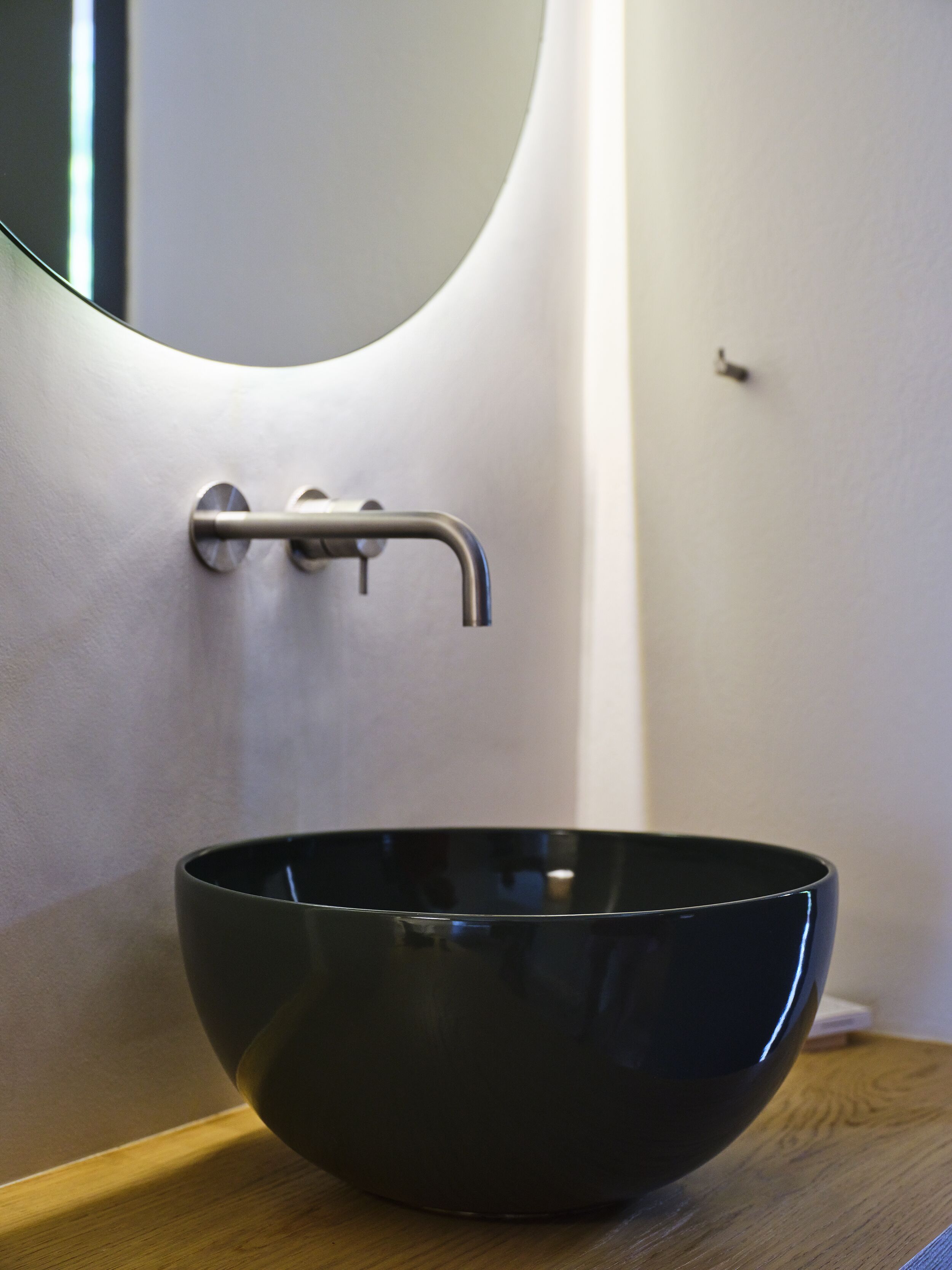 Un baño moderno con un lavamanos negro tipo recipiente sobre una encimera de madera, un espejo curvo y un grifo de pared.