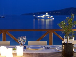 A table set for two with wine glasses and plates, overlooking a calm sea with a boat in the distance. - Sirene Blue Resort (Poros)