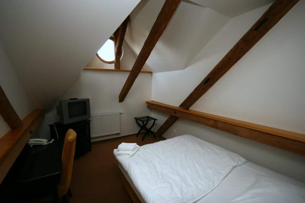 Een kleine slaapkamer onder de dakpannen met een enkel bed, een televisie en een radiator.