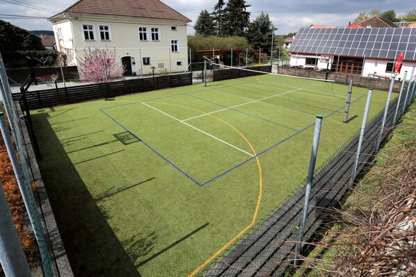 Una cancha deportiva con una red, rodeada por una valla, y casas al fondo.