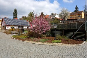 A cobblestone street with a solar panel-equipped building, a flowering tree, and a fence with a metal gate. - Hotel U Zeleného stromu (Nepomuk)
