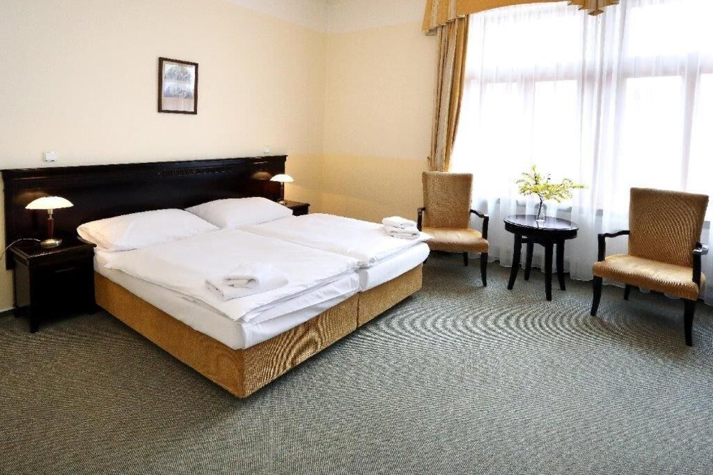 Habitación de hotel con cama doble, dos mesitas de noche, una silla, una mesita redonda y una planta en maceta.
