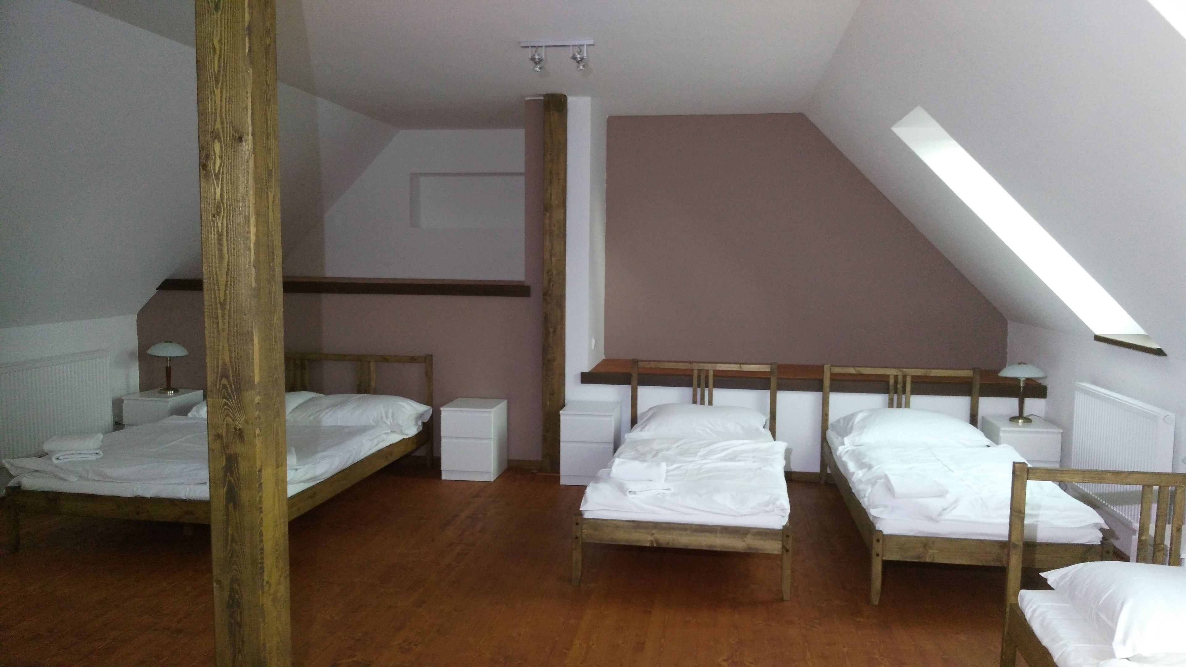 A dormitory room with three wooden bunk beds, white bedding, and a sloped ceiling with skylight.