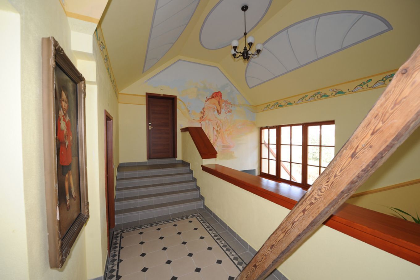 Una scala con corrimano in legno e pavimento decorato, che conduce a una stanza con una porta e una finestra.