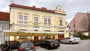 Un hôtel à la façade jaune, doté de nombreuses fenêtres et d’un espace extérieur aménagé avec des sièges, protégé par un auvent.