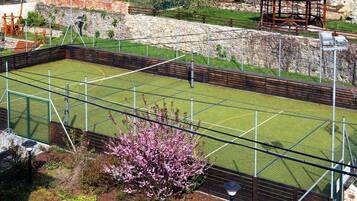 Una cancha de tenis con valla perimetral, un pabellón y un muro de piedra al fondo.