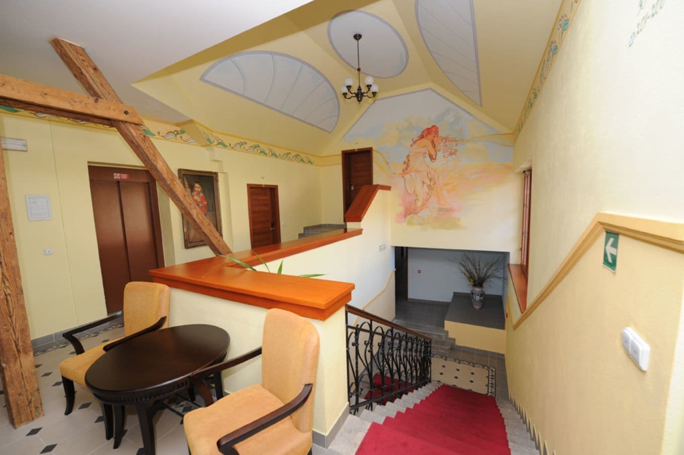 A hotel lobby with a wooden staircase, a dining area with a table and chairs, a fireplace, and a mural on the wall.