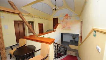 A hotel lobby with a wooden staircase, a dining area with a table and chairs, a fireplace, and a mural on the wall.