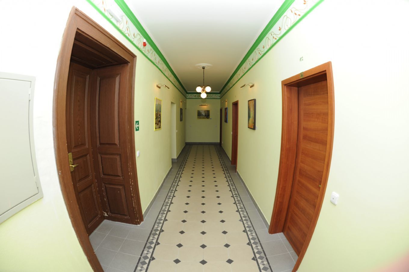 Un pasillo con baldosas de diseño, puertas de madera y luces en la pared.