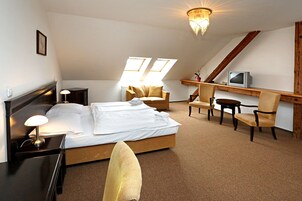 Un dormitorio con cama, mesita de noche, lámpara y televisor sobre una estantería de madera.