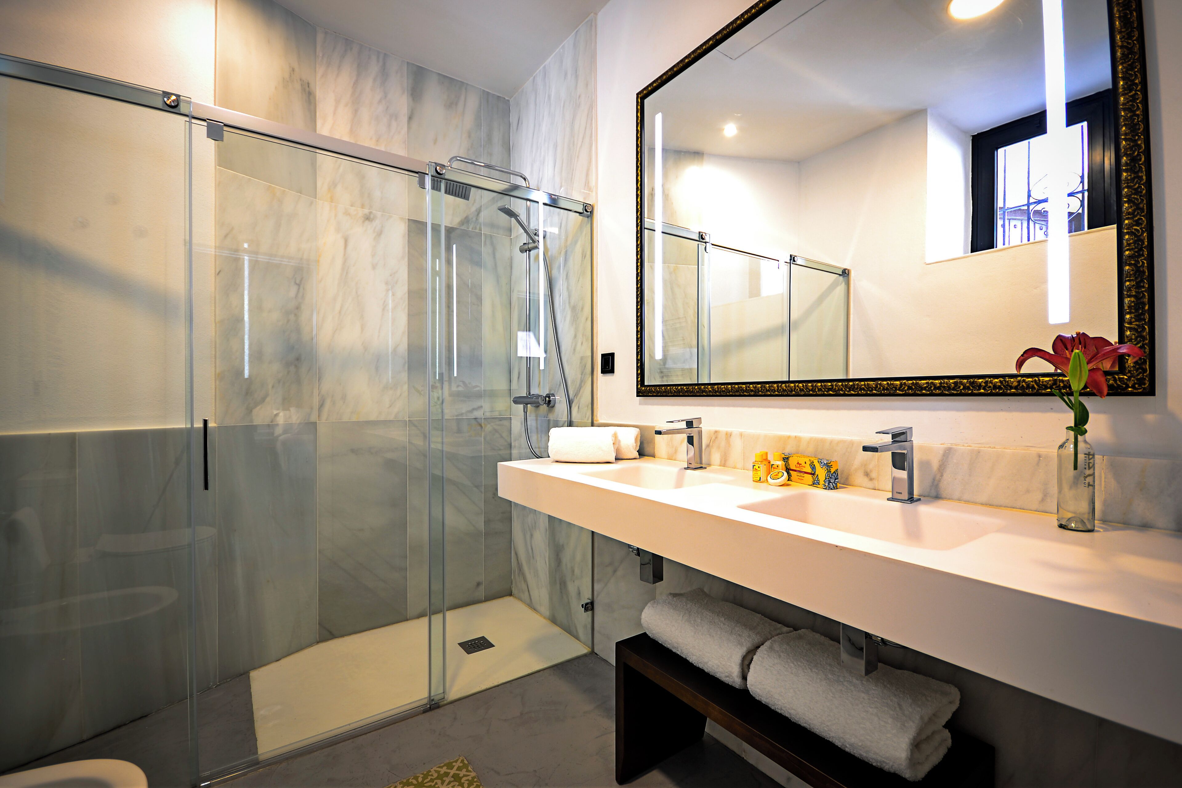 Een moderne badkamer met een douchecabine van glas, een grote spiegel en een wit wastafelmeubel met een handdoekhouder.