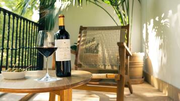 A table with a bottle of wine and a glass on a wooden table, surrounded by wicker furniture and a palm tree in the background.